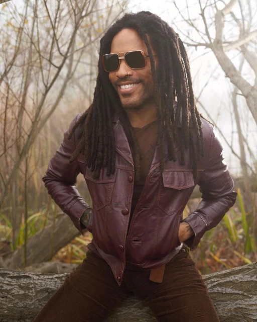 Portrait of smiling adult male with dreadlocks, wearing sunglasses and a burgundy leather jacket, sitting on a log in a misty forest.