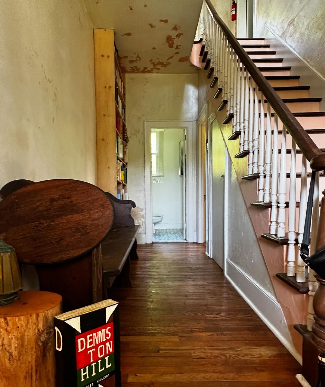 Hallway with wooden floors and staircase, bookshelf, decorative table, and interior design details in warm, inviting light.