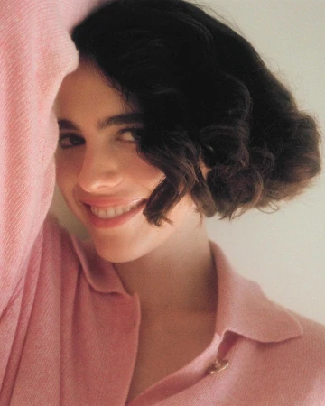 Close-up portrait of a smiling woman with short dark hair wearing a pink collared shirt, photographed by Melodie Mcdaniel