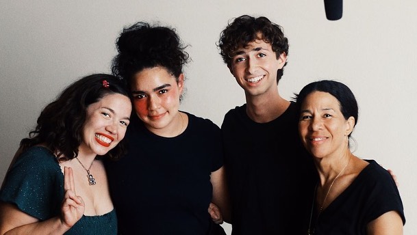 Studio shot of four people: two adult females, one adult male, and one older female, all smiling against a white backdrop.