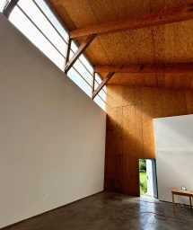 Interior of an industrial studio space with wooden beams, osb wall panels, concrete floor, and large clerestory windows.