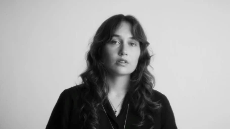 Portrait of a woman with long dark wavy hair wearing a dark shirt against a seamless white background.