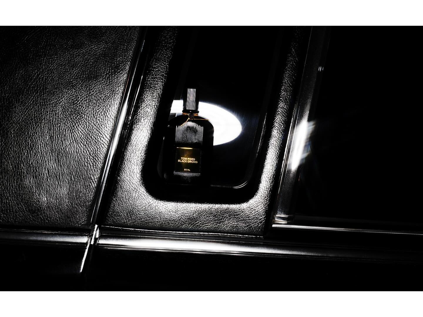 Tom Ford Black Orchid perfume bottle on textured black surface with ambient light and reflections, showcasing its luxurious design.