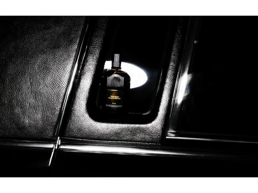 Tom Ford Black Orchid perfume bottle on textured black surface with ambient light and reflections, showcasing its luxurious design.