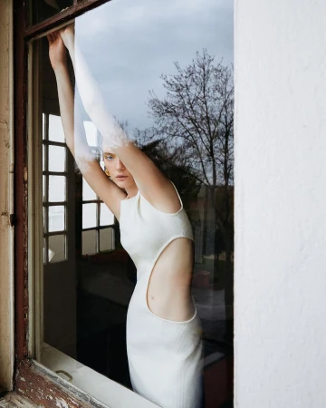Woman in a white sleeveless cut-out dress posing inside a window frame by Memet Erol
