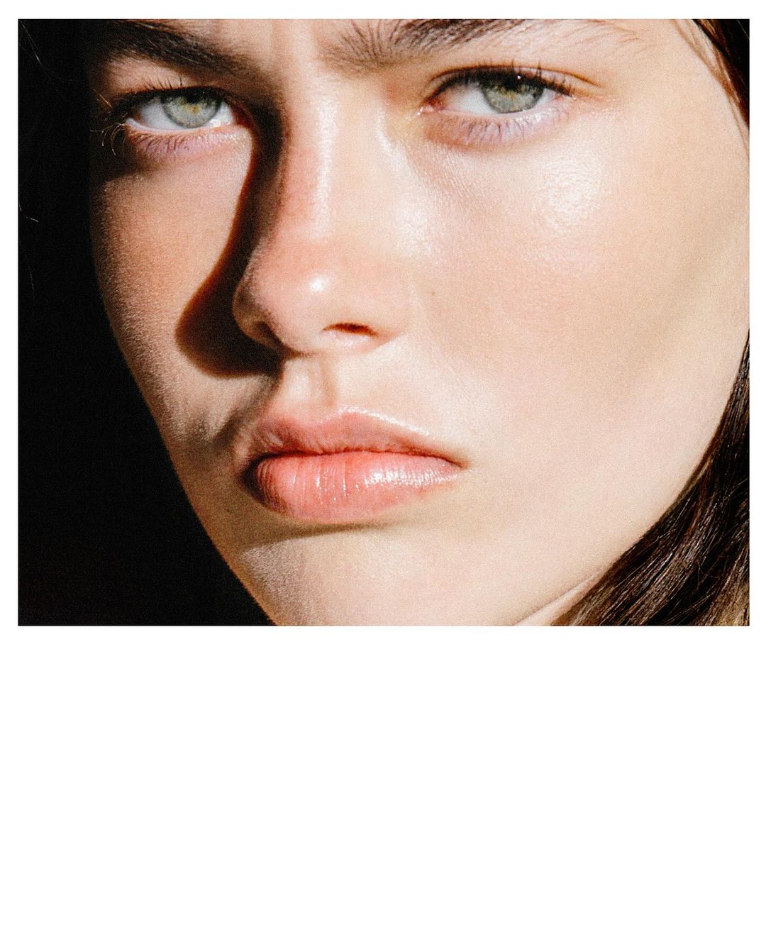Close-up beauty shot of a fair-skinned young adult female with green eyes, illuminated by natural light, against a dark background.