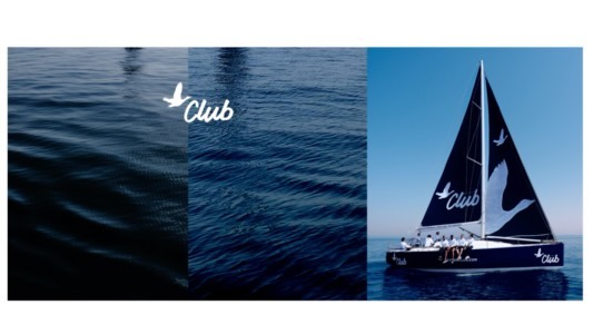 Sailboat with group of people sailing on the water under a clear blue sky, branded with a logo; promoting water travel.