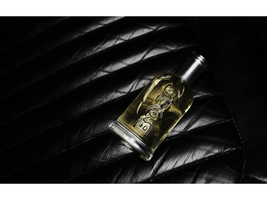 Boss Bottled Eau de Toilette fragrance bottle on a textured black surface, showing the bottle's clear glass and silver cap design.