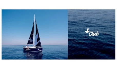 A sailboat with black and white sails sailing on calm blue ocean water with a white bird logo and text on the sail.
