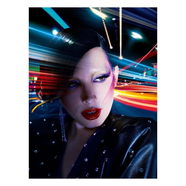 Glamorous portrait of an adult woman with red lipstick and a jeweled jacket against a blurred, colorful, long-exposure-like background.