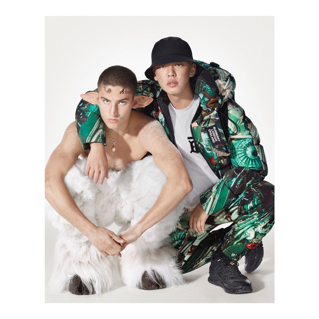 Two men pose in a studio: one is wearing a green patterned jacket and a black hat, the other is wearing a faun costume.
