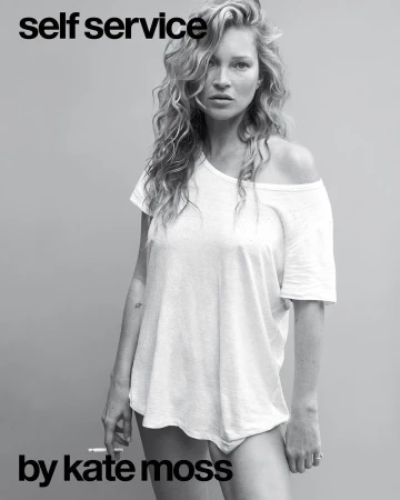 Kate Moss poses in a black-and-white portrait, wearing a white t-shirt, with curly blonde hair and a cigarette in her left hand.