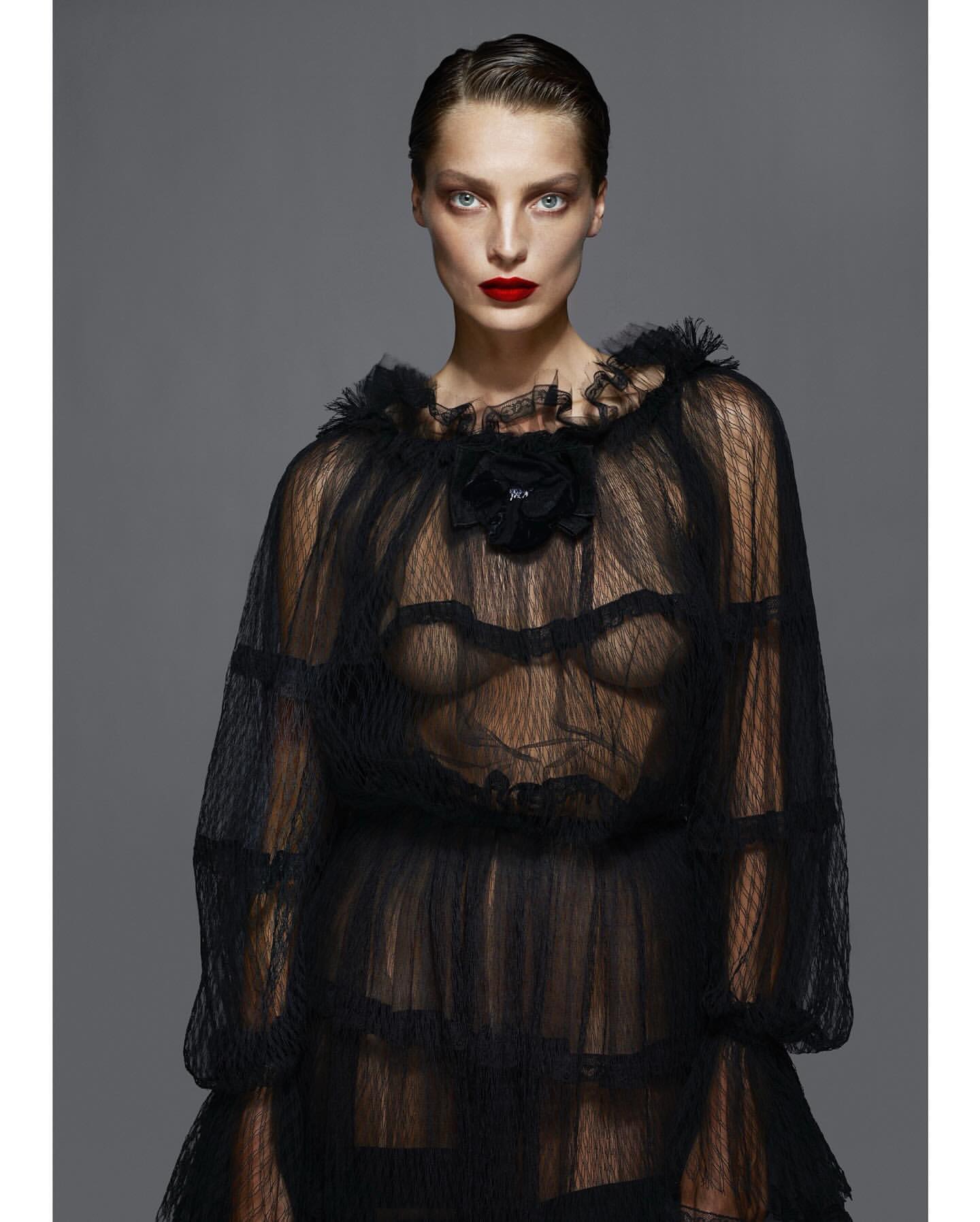 Fashion portrait of a woman with red lipstick wearing a frilled black net dress against a grey background in a photo studio.