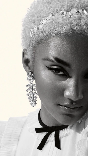 Close-up portrait of a Black woman with platinum blonde hair and statement earrings, wearing a black ribbon choker and white collared shirt.