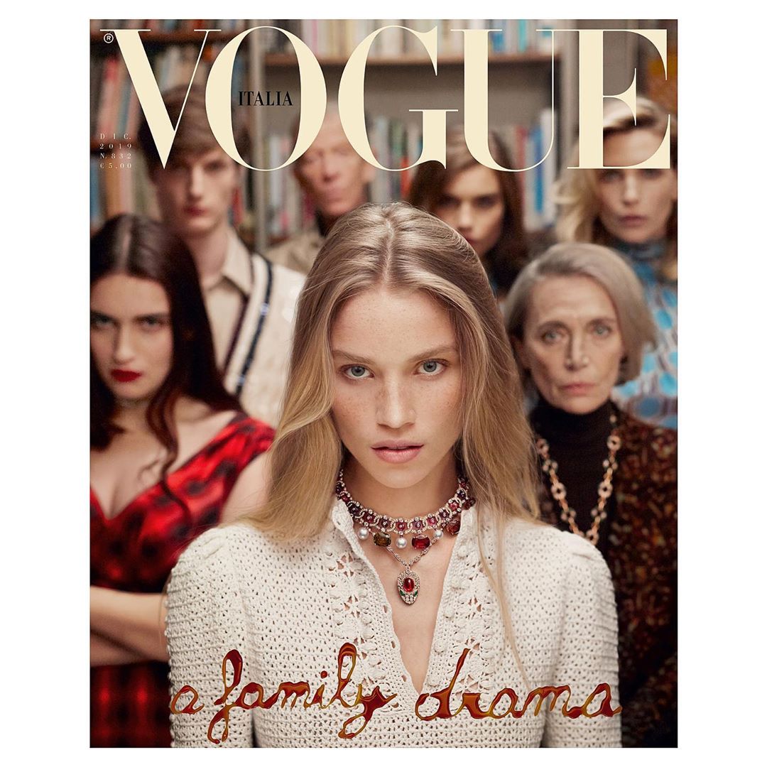 Vogue Italia cover features a fair-skinned woman in white crochet sweater and jewelry, surrounded by a group of diverse people and books.