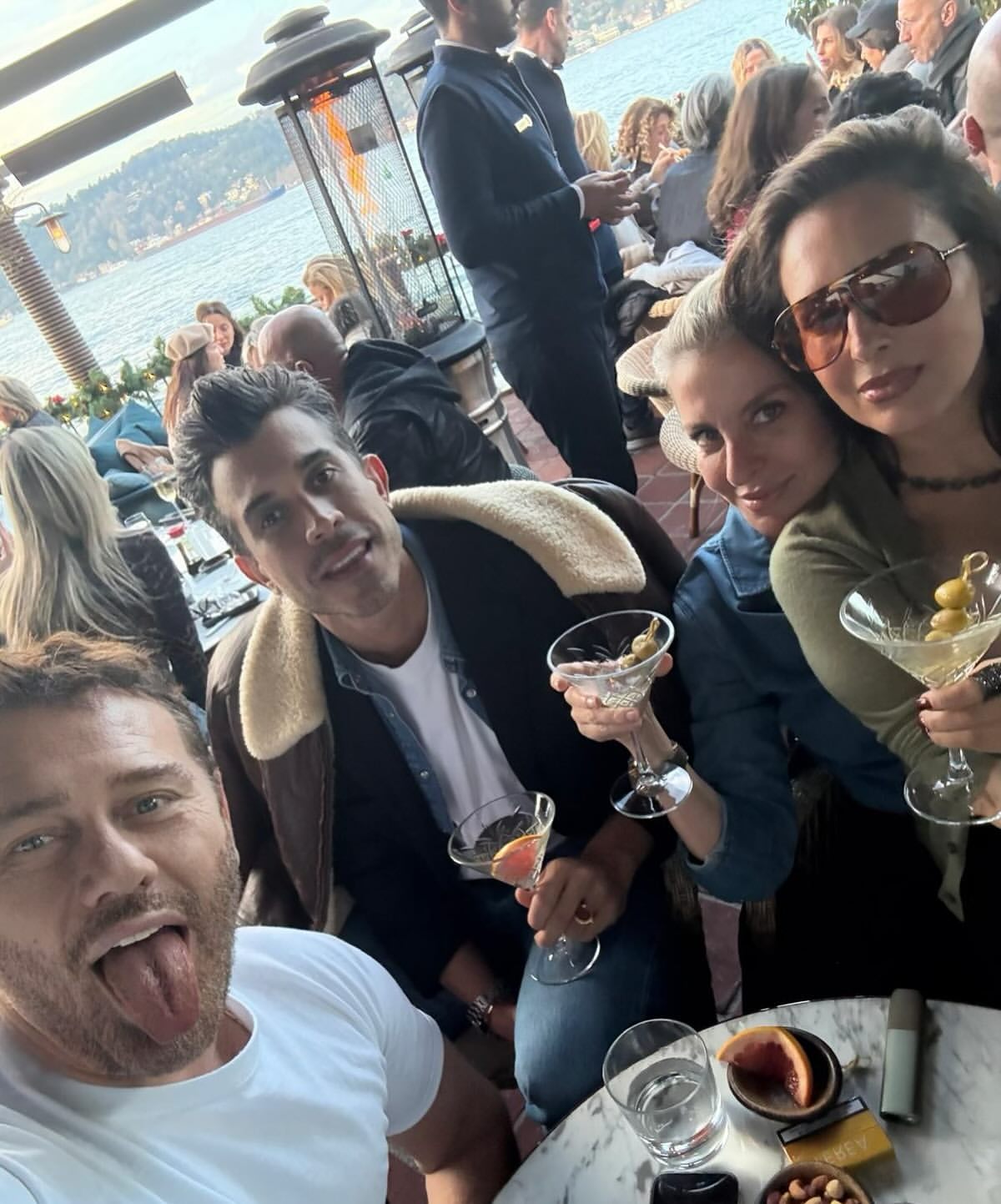 Group of friends enjoying cocktails outdoors with an ocean view backdrop; people are smiling and holding martini glasses.