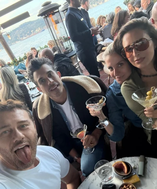 Group of friends enjoying cocktails outdoors with an ocean view backdrop; people are smiling and holding martini glasses.