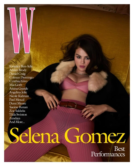 Selena Gomez poses on a mustard-colored couch for a magazine cover, wearing a pink bra top, pleated trousers, and a fur-collared coat.