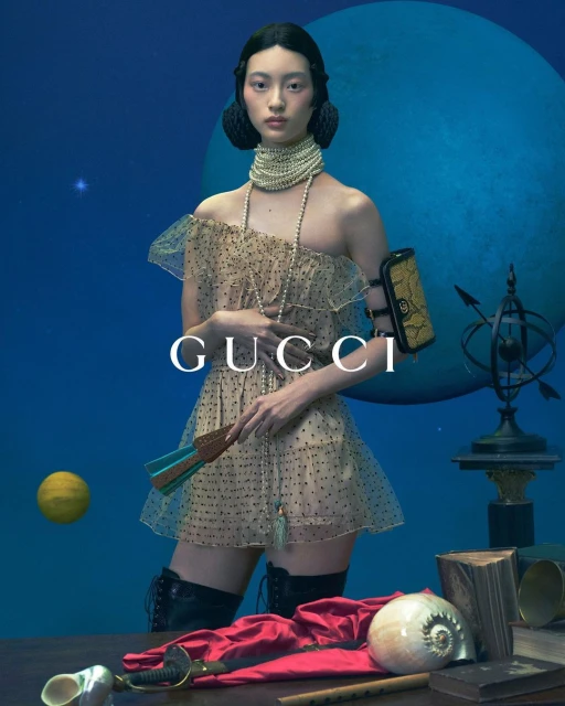 Asian woman in tulle dress posing in front of blue globe with fashion accessories for Gucci fashion editorial advertisement.