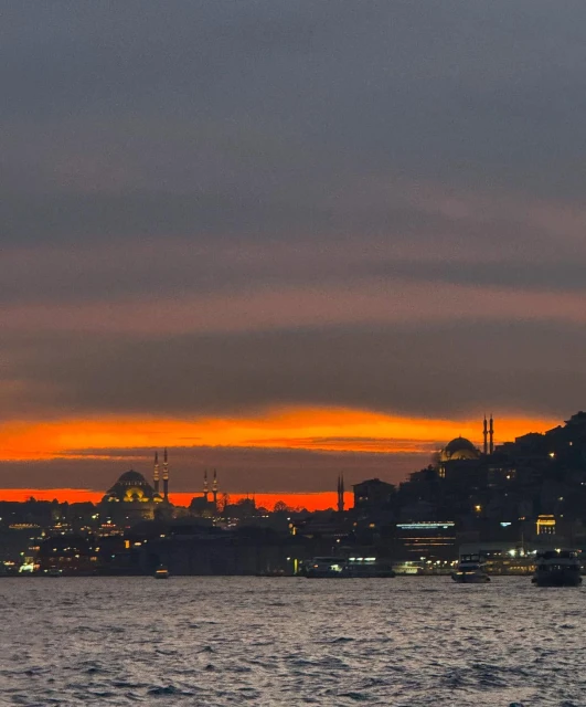 City skyline at dusk with silhouettes of mosques and buildings along the water, lit by the colorful glow of the setting sun.