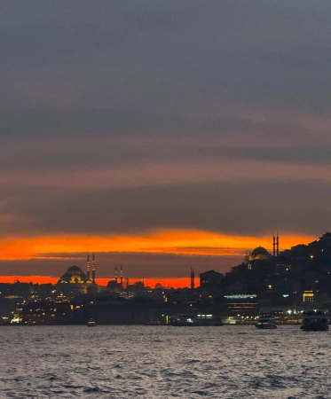 City skyline at dusk with silhouettes of mosques and buildings along the water, lit by the colorful glow of the setting sun.