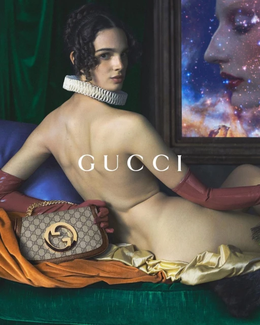 A model poses with a Gucci handbag on a green velvet surface, accessorized with long gloves and a ruffled collar, next to an art piece.