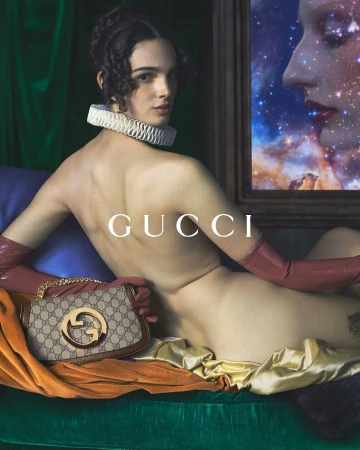 A model poses with a Gucci handbag on a green velvet surface, accessorized with long gloves and a ruffled collar, next to an art piece.