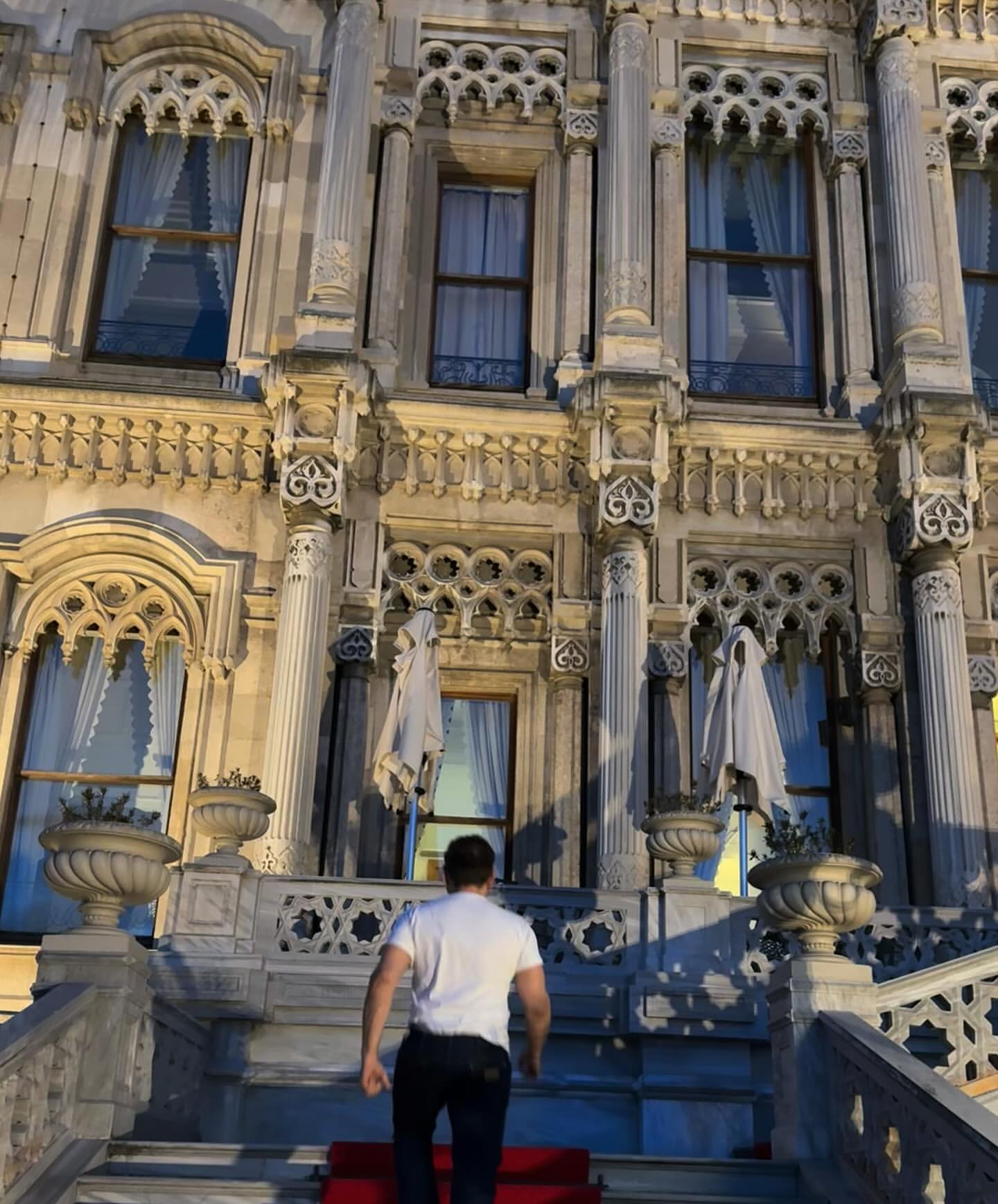 Man ascends ornate staircase of Dolmabahçe Palace in Istanbul. Ornate columns, windows, and a red carpet enhance the architectural detail.