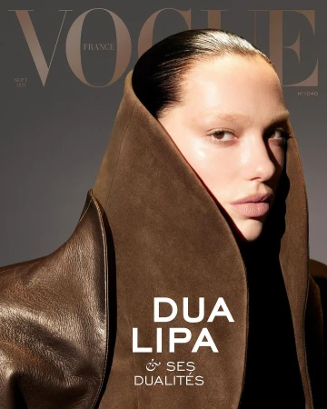 Close-up portrait of Dua Lipa wearing a structured brown hooded leather coat against a grey background.