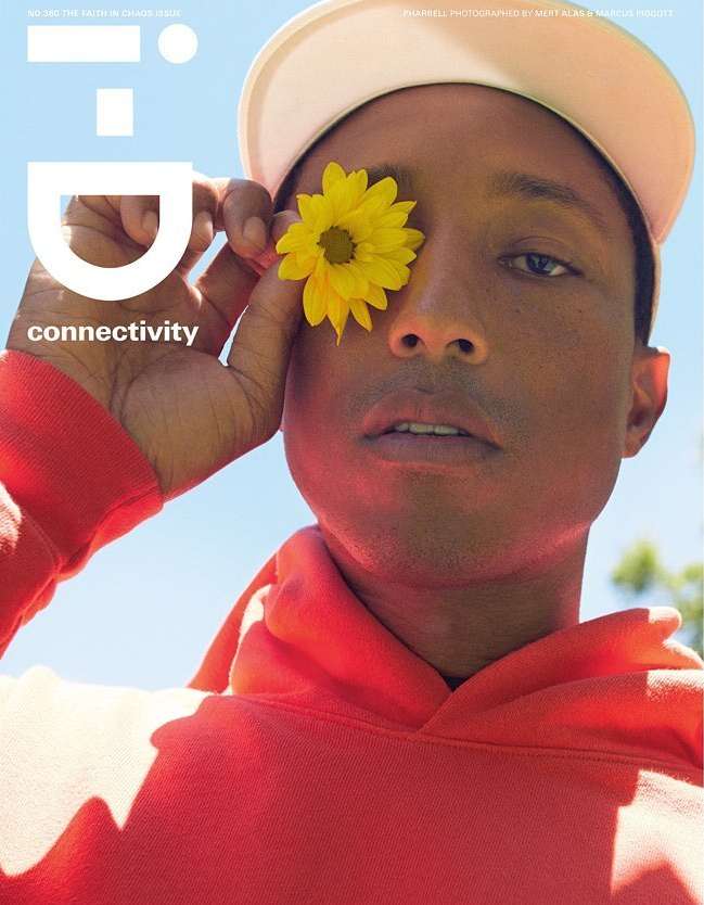 Magazine cover featuring a man in an orange hoodie and white hat holding a yellow flower to his eye against a blue sky.