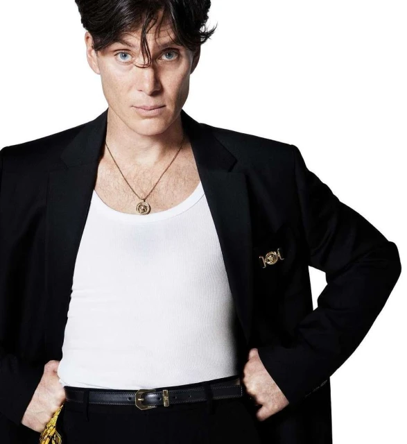 Headshot of Cillian Murphy in a black suit jacket over a white tank top with a gold necklace posing against a white backdrop.