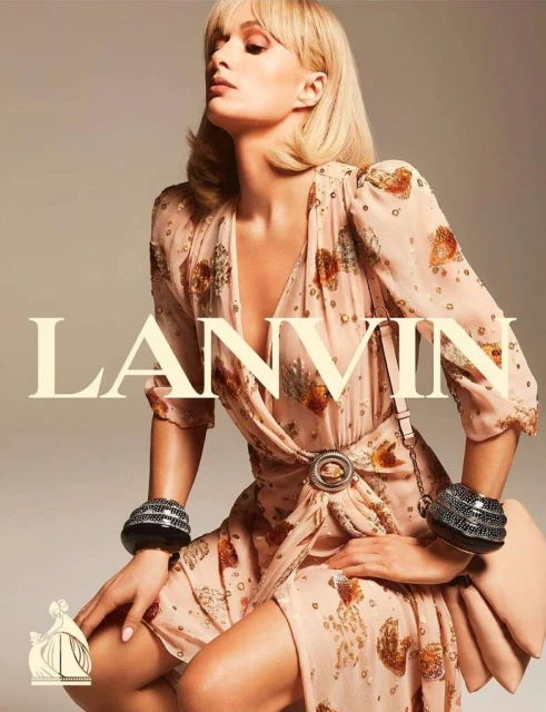 A woman in a patterned dress with dark bracelets poses in front of a light beige background. The LANVIN logo is visible to the left.