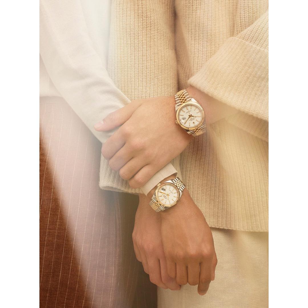 Close-up of two people wearing gold and silver watches, hands clasped, showcasing fashion accessories and luxury timepieces in neutral tones.
