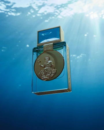 Elegant product shot of a clear blue glass perfume bottle with gold accents and embossed figure of Poseidon against a blurred blue underwater background.