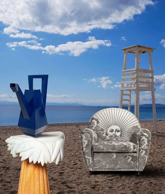 Surreal beach scene featuring a blue watering can sculpture on a marble base, a patterned armchair, and a lifeguard tower under a blue sky.