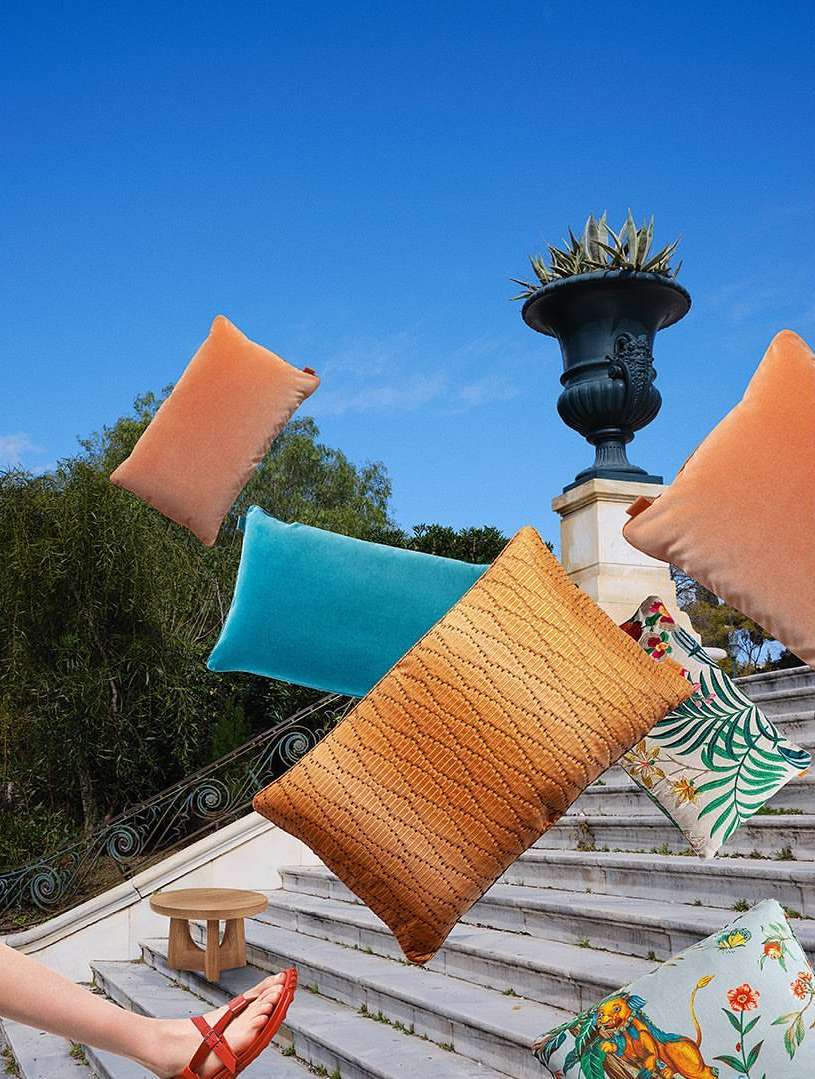 Various colorful cushions floating on stone steps against a blue sky, foot in red sandal visible, and landscape architectural element.