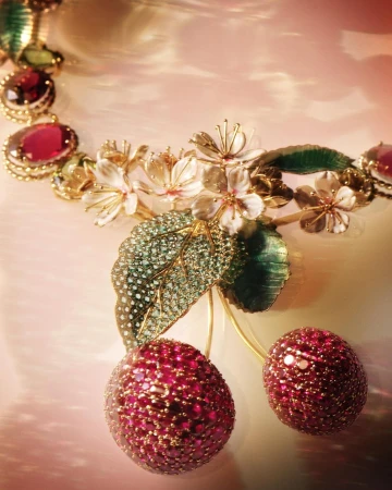 Close-up of an elaborate golden necklace featuring cherry and floral designs, adorned with pink gemstones and set against a soft backdrop.