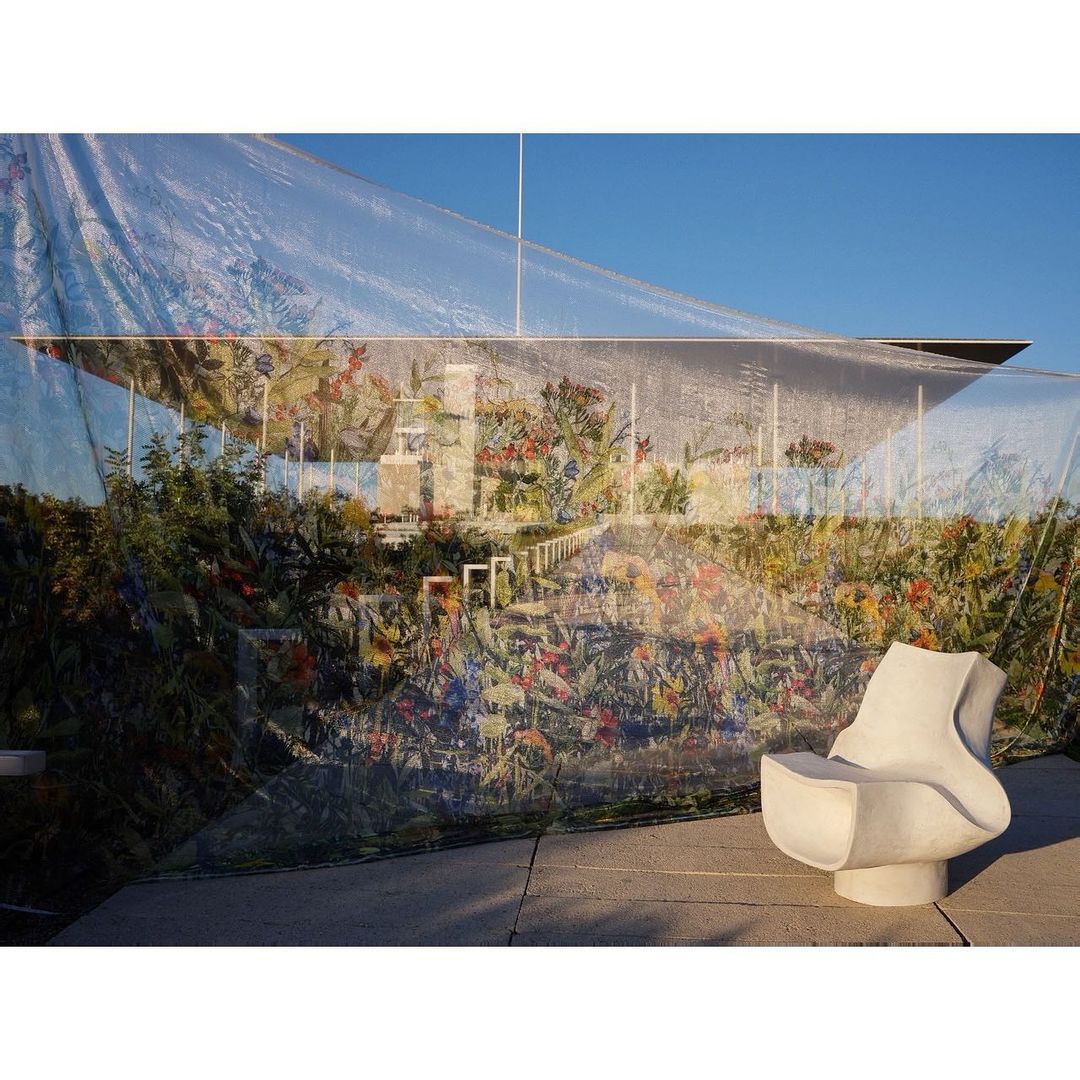 Modern architectural building covered in floral print tarp with a sculptural white chair in the foreground on a sunny day.