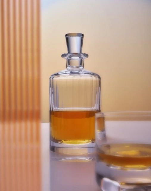 Crystal decanter with amber liquid and glass on a reflective surface against an orange gradient background, showcasing glassware elegance.
