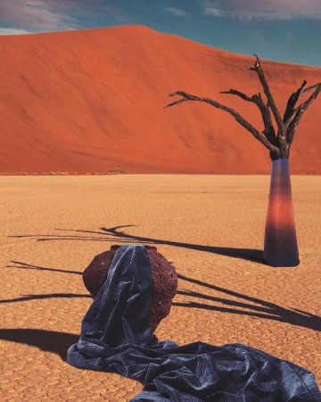 Striking desert landscape featuring a dead tree in a vase, draped fabric, and a large sand dune under a clear blue sky.