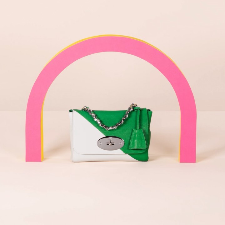 Green and white Mulberry handbag with silver chain strap against a pale background, framed by a pink and yellow semi-circular arch.
