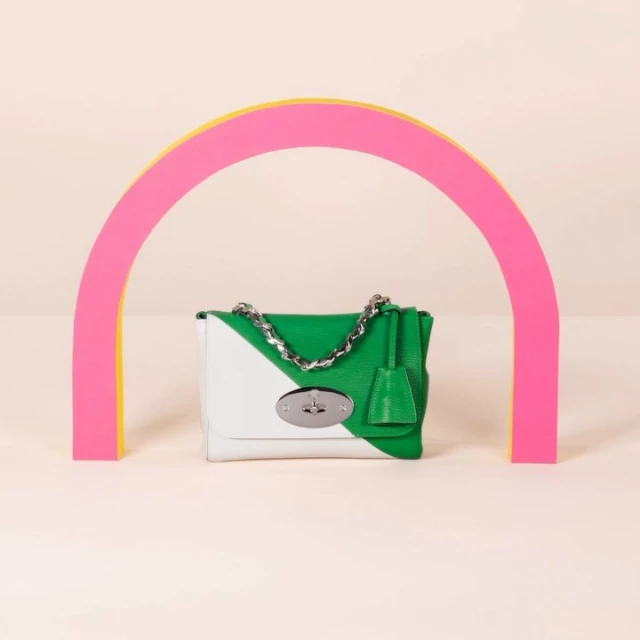 Green and white Mulberry handbag with silver chain strap against a pale background, framed by a pink and yellow semi-circular arch.