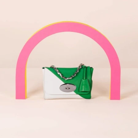 Green and white Mulberry handbag with silver chain strap against a pale background, framed by a pink and yellow semi-circular arch.