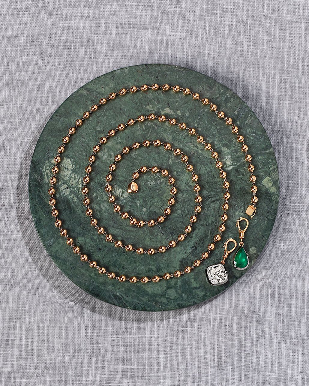 Elegant gold beaded necklace with gemstone pendants on a round green marble tray, set against a light gray linen backdrop.