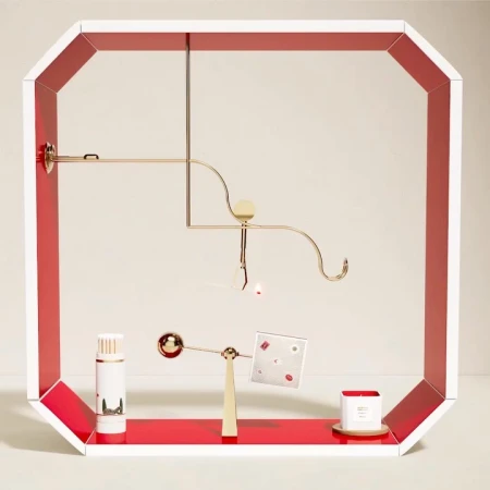 Abstract product display featuring cylindrical bottles, candle, and geometric shapes in a white and red frame against a neutral backdrop.