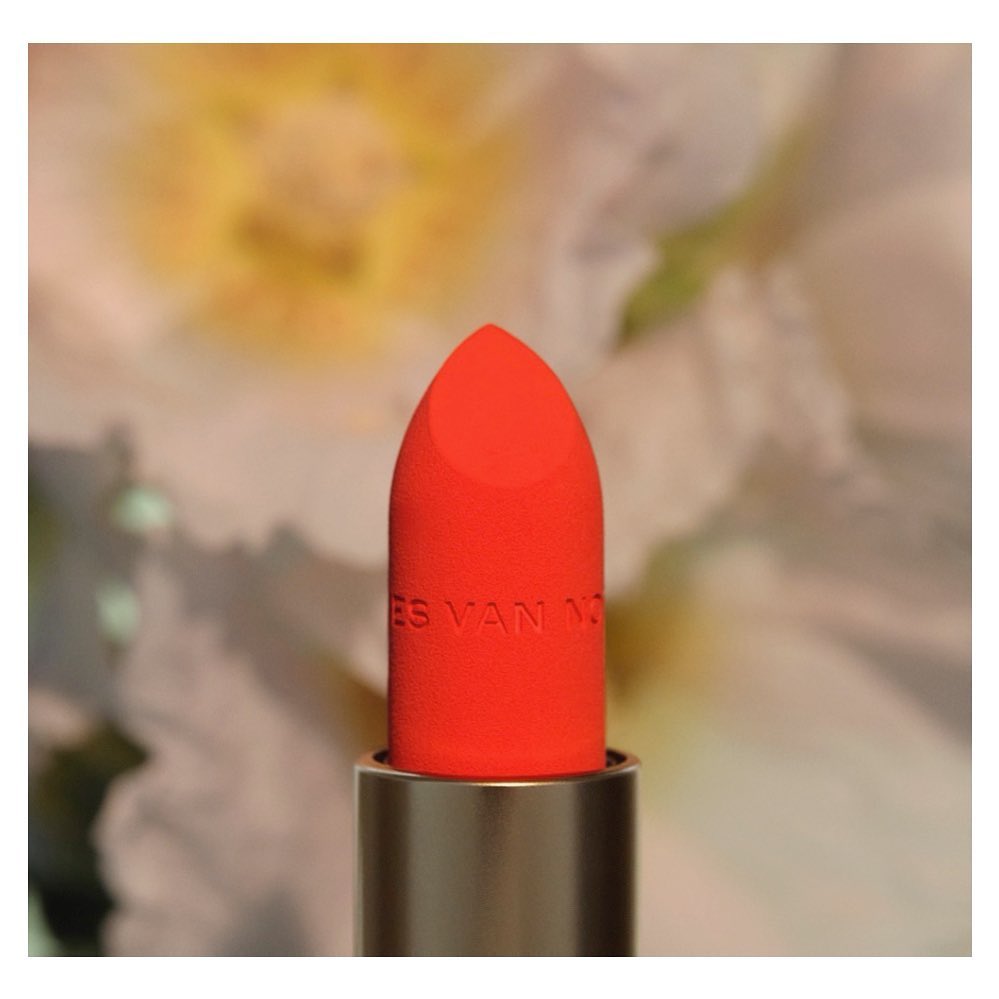 Close-up of vivid orange lipstick, showcasing its texture and color against a soft floral backdrop for beauty and cosmetic promotion.