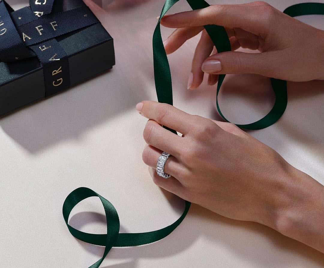 Close-up of a woman's hands holding a dark green ribbon, featuring a diamond ring and a black gift box with a GRAFF logo.