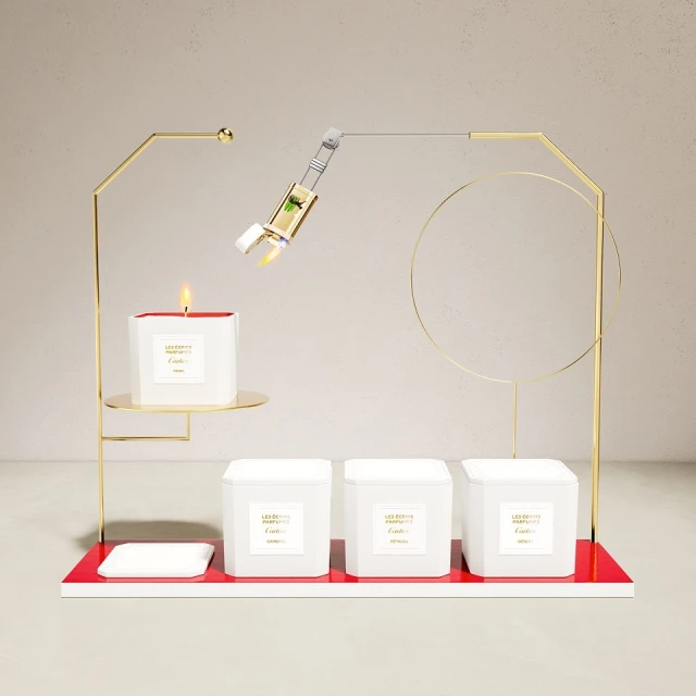 Elegant product shot of candle and fragrance bottle atop geometric gold display stand on an off-white surface against a plain backdrop.