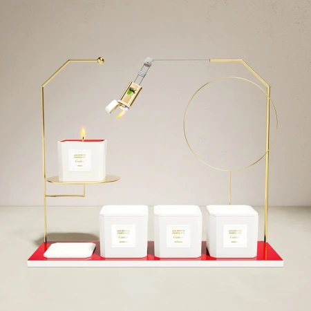 Elegant product shot of candle and fragrance bottle atop geometric gold display stand on an off-white surface against a plain backdrop.
