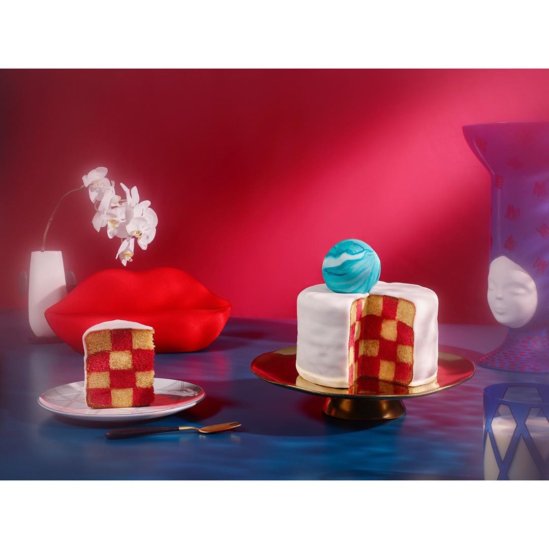 Artfully arranged checkerboard cakes with white frosting, blue marble topping, modern art vases, and a vibrant red and blue backdrop.